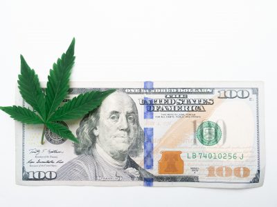 A cannabis leaf on top of a United States hundred-dollar currency bill.