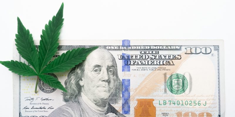 A cannabis leaf on top of a United States hundred-dollar currency bill.